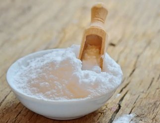 A bowl of baking soda with a wooden spoon resting on top, ready for use in baking or cooking